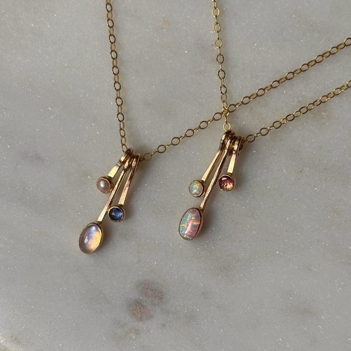 gemstone drop necklaces in gold on a marble background with blue and pink stones