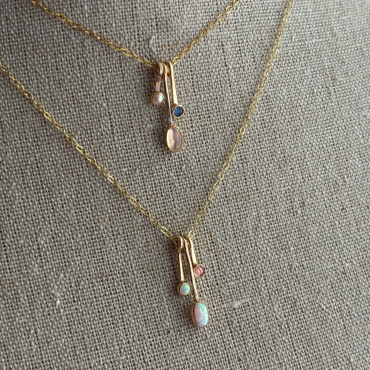 gemstone drop necklaces in gold on a textured fabric background