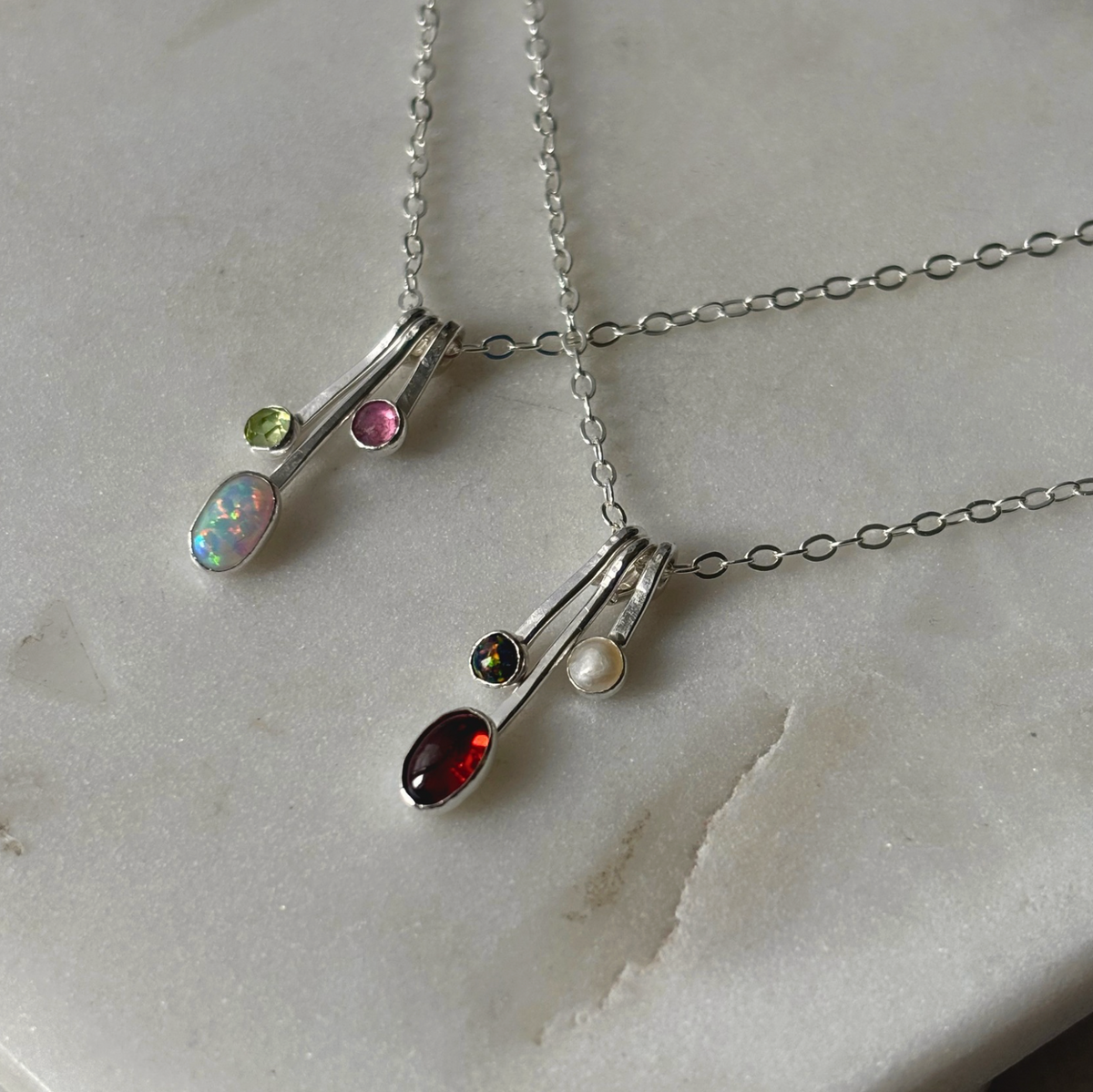gemstone drop necklaces in silver on a marble background