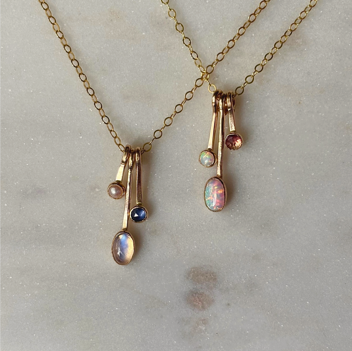 gemstone drop necklaces in gold on a marble background