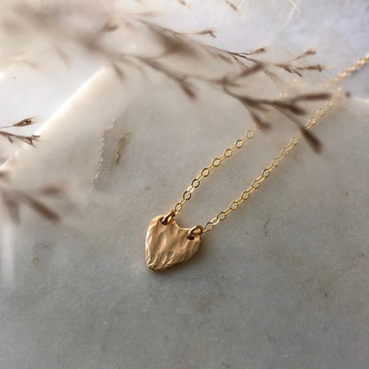 A textured gold heart shaped pendant on a marble background.