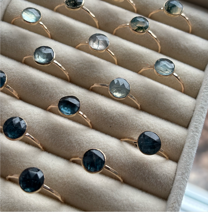 Jewelry display with rings featuring gemstones on a beige cushion.