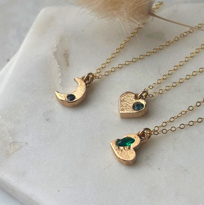 Gold necklaces with heart and crescent moon pendants on a marble surface