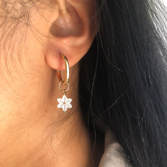 A Mother of Pearl charm flower dangling from a gold hoop earring.
