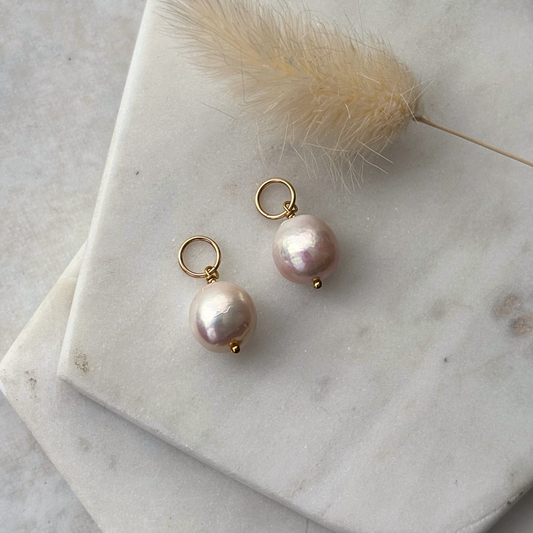 Pearl charms on a marble surface with a dried plant