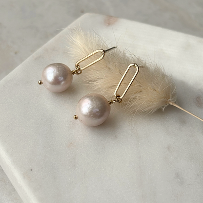 Pearl earrings with gold hooks on a marble surface with a feather.