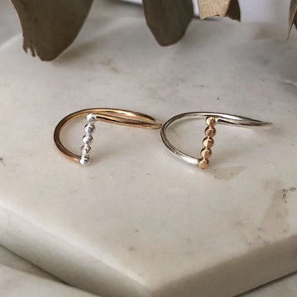 Two rings, one with a gold band and silver accents, and another with a silver band and gold accents, placed on a marble surface.
