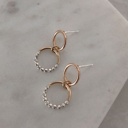 Gold-colored hoop earrings with a textured surface on a marble background.