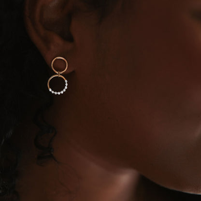 A close-up image of a person wearing a gold-colored hoop earring with a textured surface.