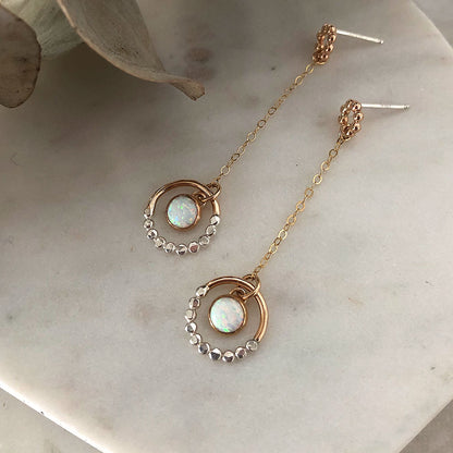 A pair of mixed metal opal dangle earrings on a marble background.