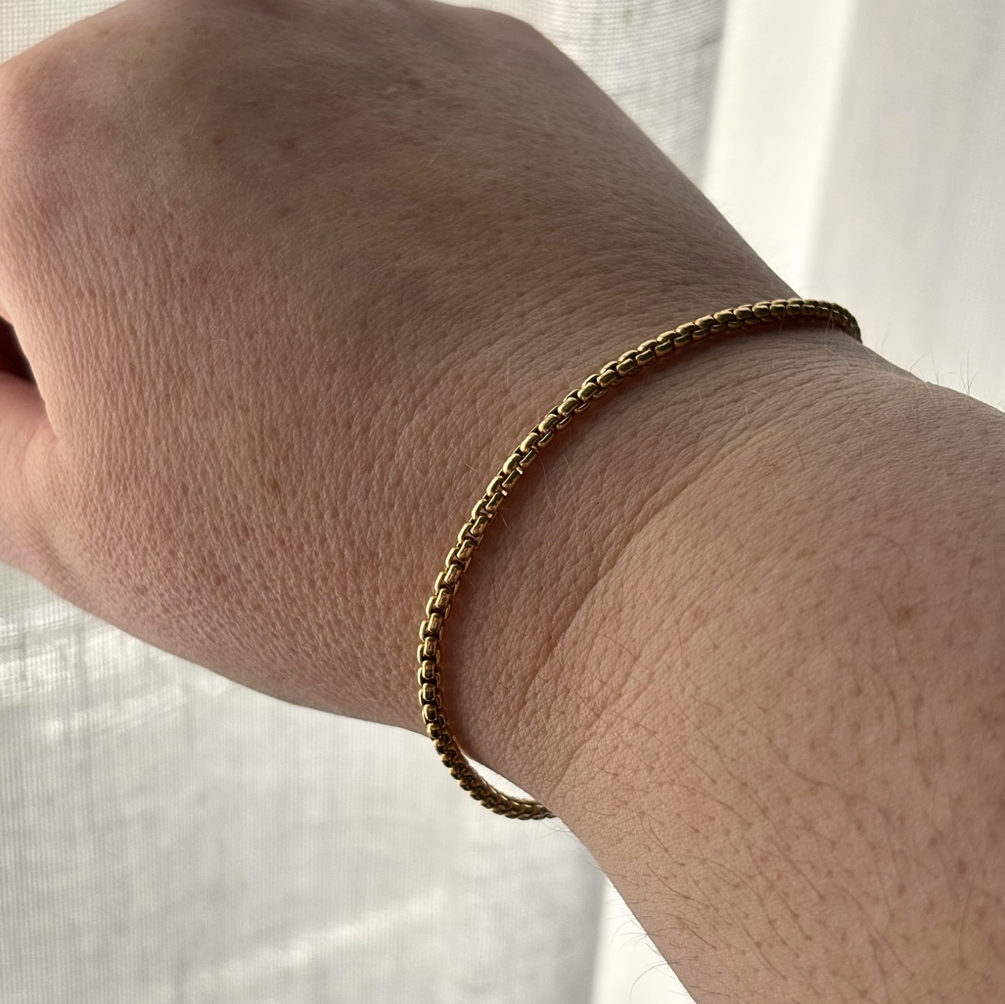 Gold bracelet on a wrist with a light background