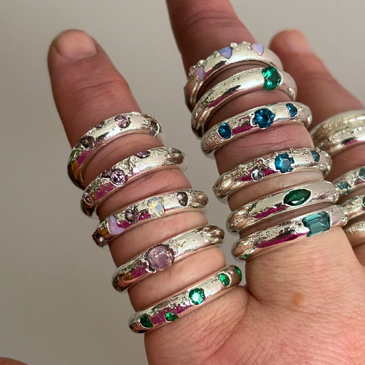 Multiple silver rings with gemstones on a finger against a neutral background