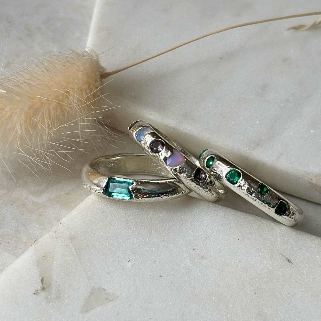 Three chunky silver rings with embedded gemstones on a marble surface.