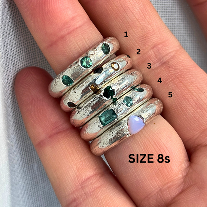 Stack of silver rings with gemstones on a hand, labeled with sizes.