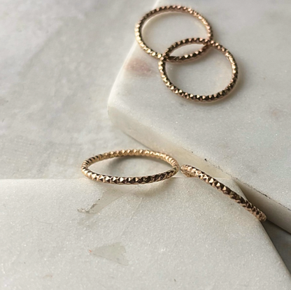 A close-up of three textured stacking rings made of 14k gold-fill, placed on a marble surface.