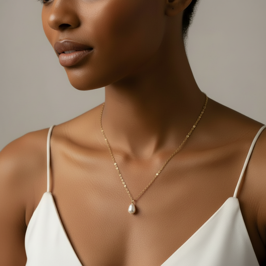 Woman wearing a gold necklace with a pearl pendant against a neutral background