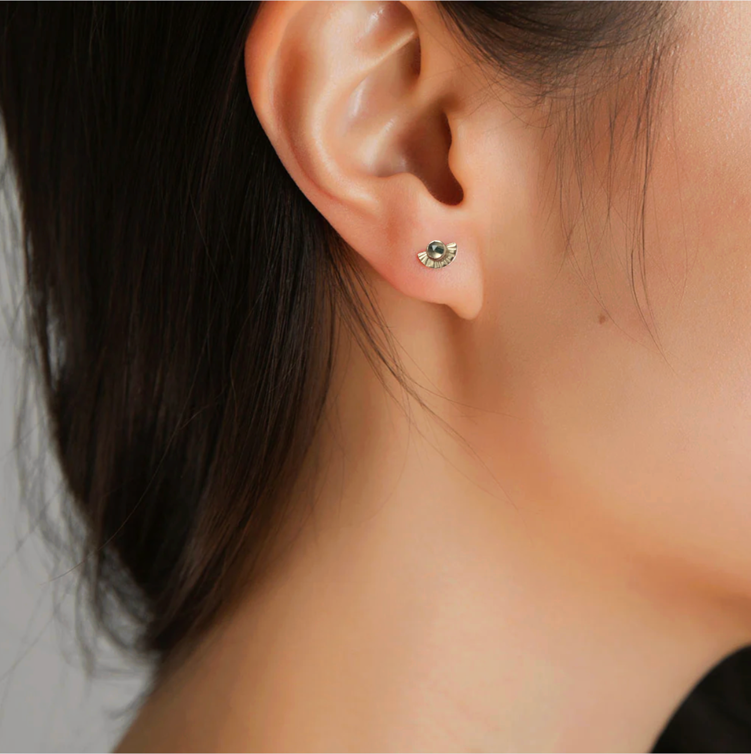 Close-up of an ear wearing a small earring with a neutral background