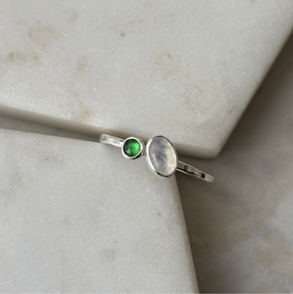 silver toi et moi ring with moonstone and emerald on a marble background