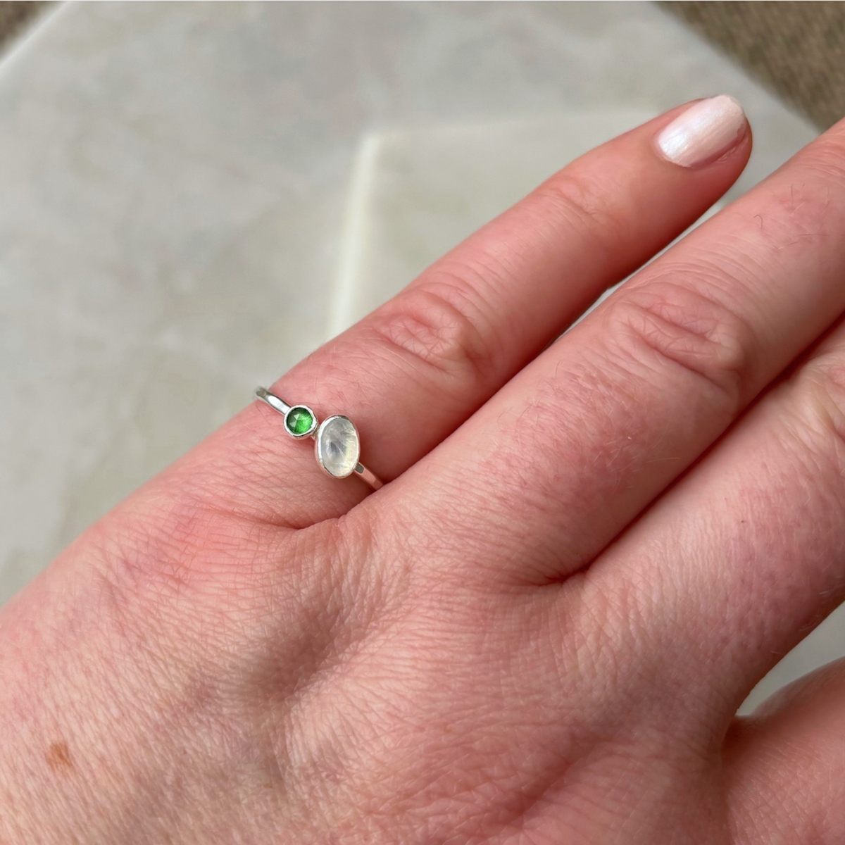 silver toi et moi ring with moonstone and emerald on a hand