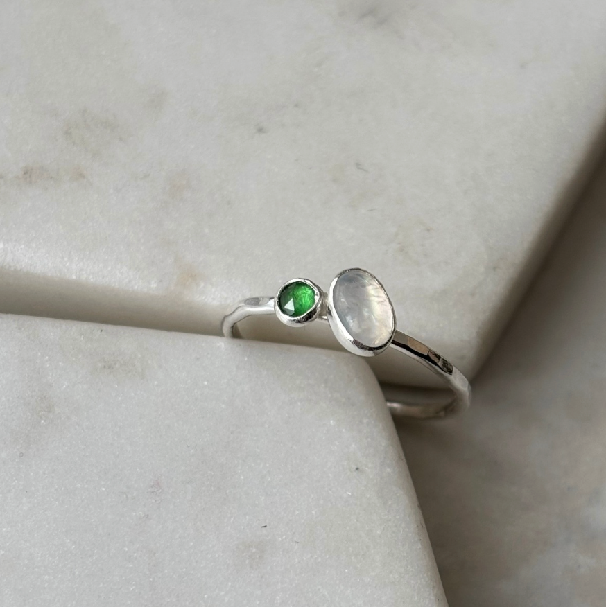 silver toi et moi ring with moonstone and emerald on a marble background