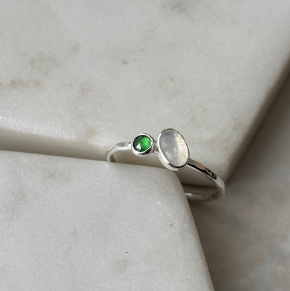 silver toi et moi ring with moonstone and emerald on a marble background
