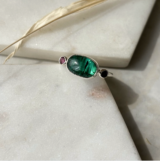 Silver ring with a green gemstone on a light stone surface