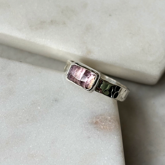 Silver ring with a pink gemstone on a marble surface