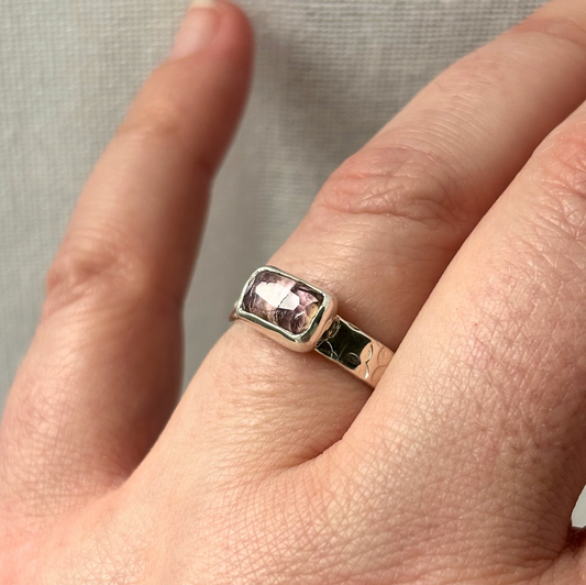 Silver ring with a pink gemstone on a finger
