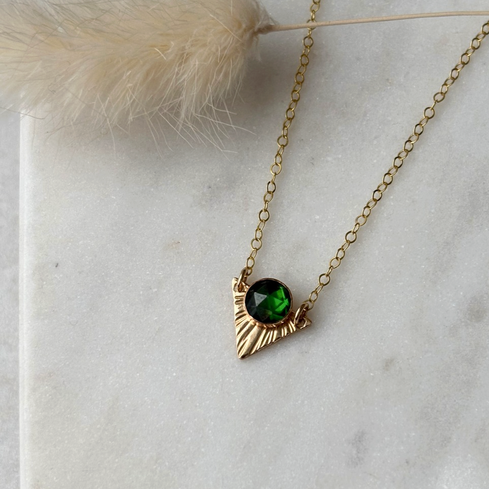 Gold necklace with a green gemstone pendant on a light marble background