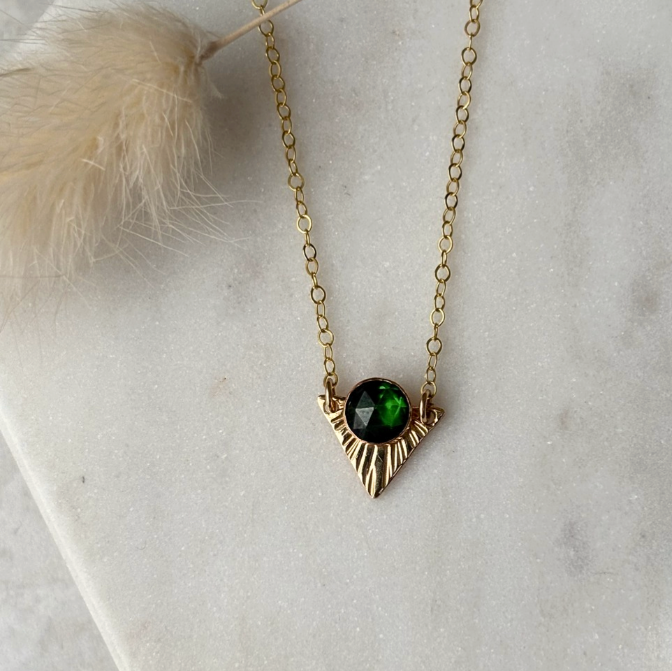 Gold necklace with a green gemstone pendant on a light gray surface.