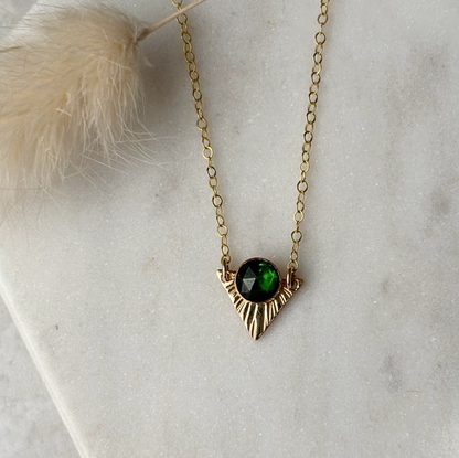 Gold necklace with a green gemstone pendant on a light gray surface.