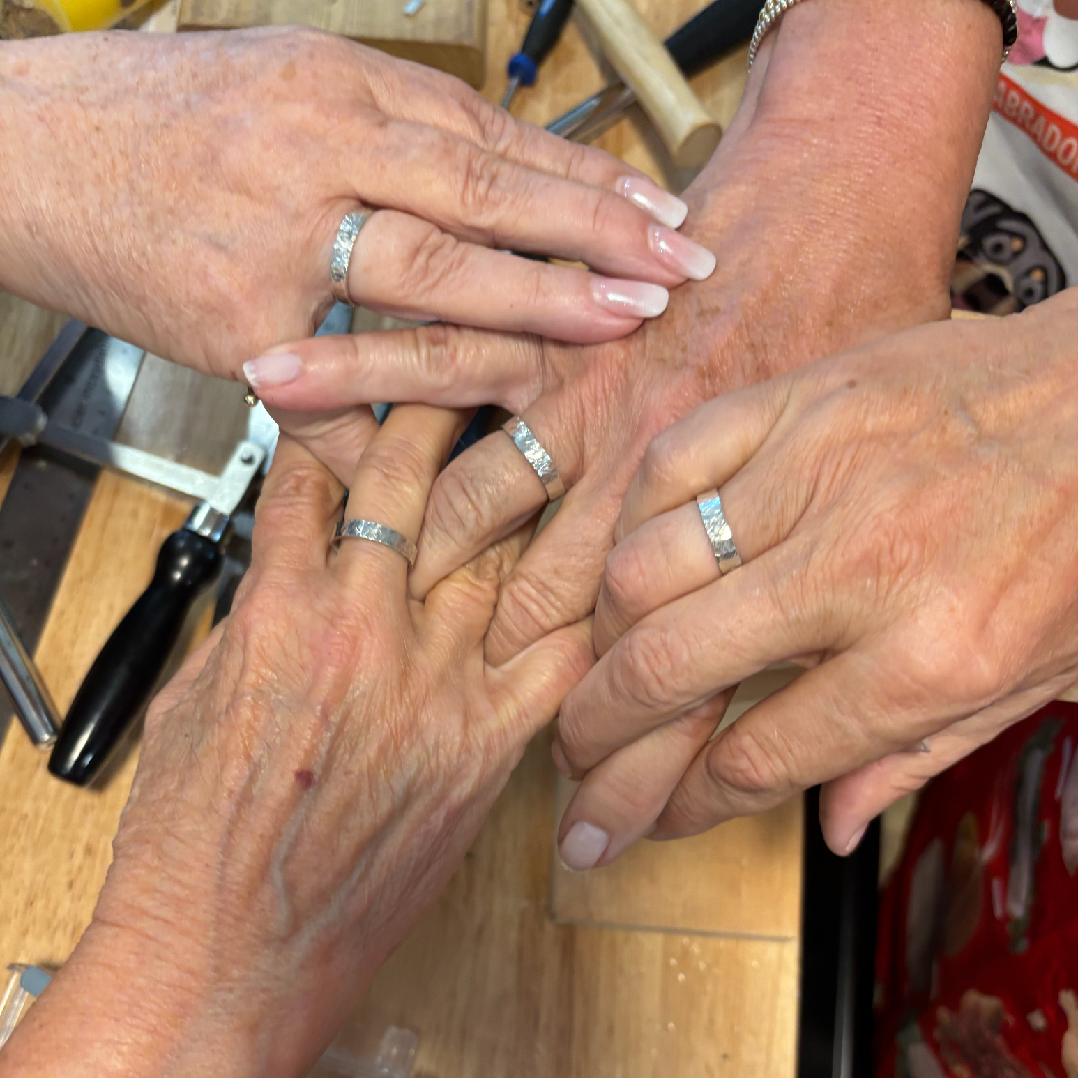 Close-up of four hands with wide silver rings rings on a wooden surface.