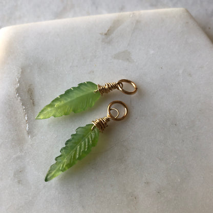 Two leaf-shaped carved aventurine charms with gold-fill wire on a marble surface.