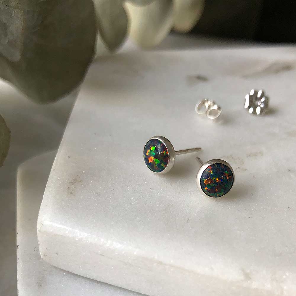 A pair of black opal stud earrings on a marble surface, with a blurred background.